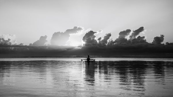 black and white photography, silhouette art, Zanzibar fishing boat, traditional pirogue, fine art monochrome, dramatic seascapes, Mnemba Island photo, African culture photography, black and white landscape, high-end wall art, sunset reflections, serene waterscape, collectible photography, timeless fine art, exclusive black and white prints, fine art seascapes