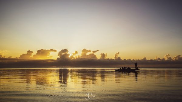 sunset photography, Zanzibar fishing boat, traditional pirogue, warm sunset reflections, golden hour photography, fine art landscape, African culture photography, Mnemba Island photos, serene coastal scenes, high-end wall art, luxury art prints, cultural traditions photography, tranquil seascape, collectible photography, limited edition artwork, sunset silhouettes